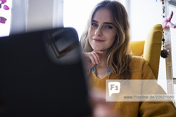 Woman in a home office smiling at the camera while using a laptop