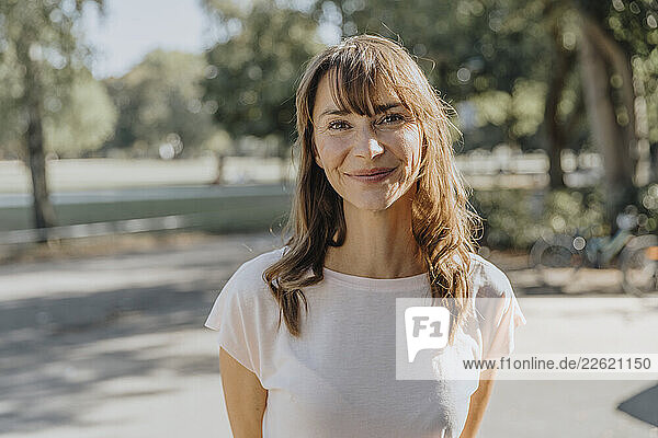 Smiling woman standing on street during sunny day