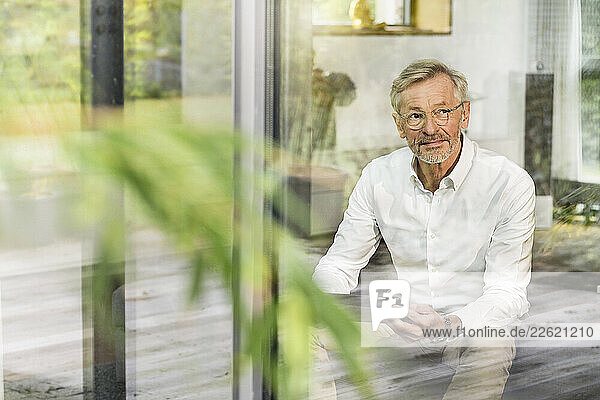 Senior man with grey hair in modern design living room with tablet sitting on couch
