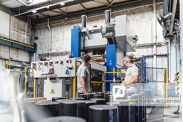 Mature male technician explaining young colleague about machine in illuminated industry