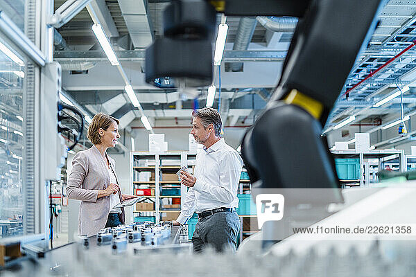 Two professionals discussing in a production hall with industrial robots