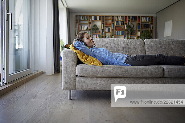 Woman wearing headphones listening music while lying on sofa at home