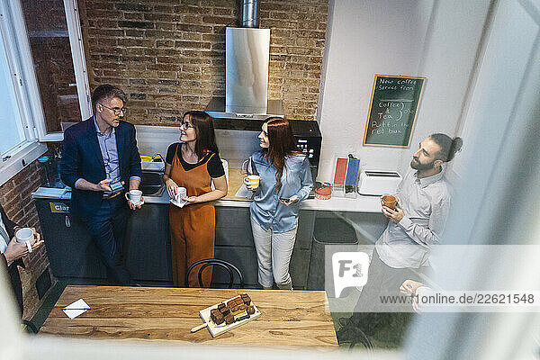 High angle view of smiling female coworkers discussing with entrepreneur while having coffee in office kitchen seen through glass window