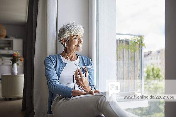 Woman at home listening to music on her phone by the window