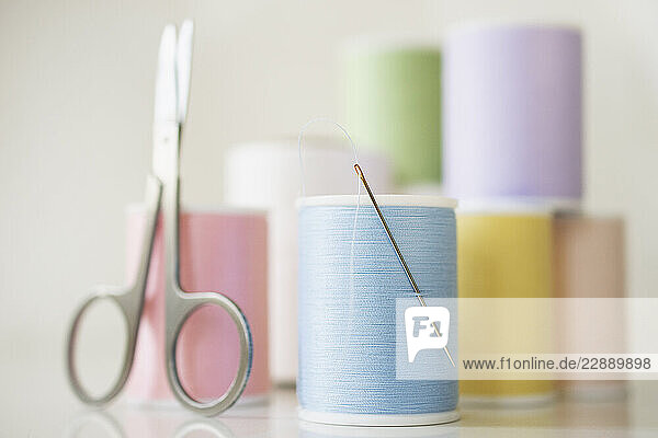 Studio shot of spools of pastel colored thread  needle and scissors