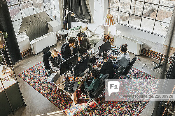 High angle view of focused multiracial IT professionals working on technologies while sitting at desk in tech hub