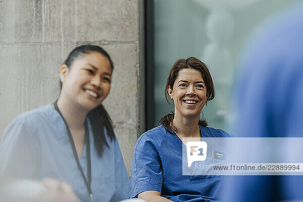 Happy female physician sitting with medical team in hospital
