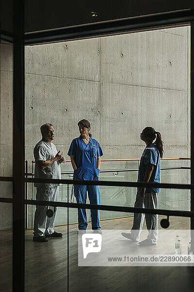 Female nurses listening to male doctor explaining while standing in hospital corridor