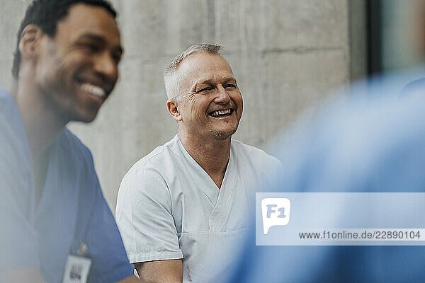 Happy mature male physician enjoying with team in clinic
