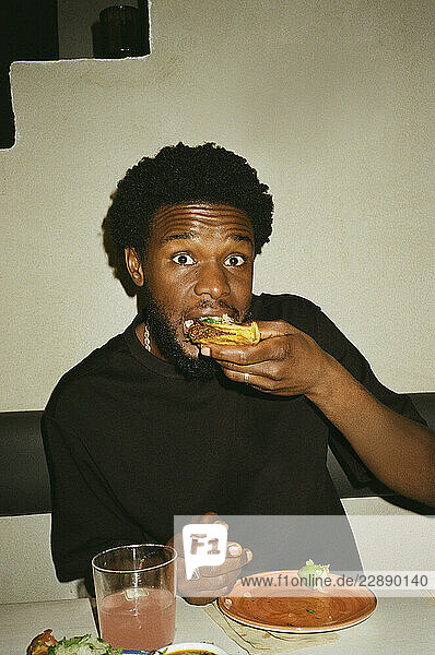 Portrait of young man eating tacos while sitting at restaurant