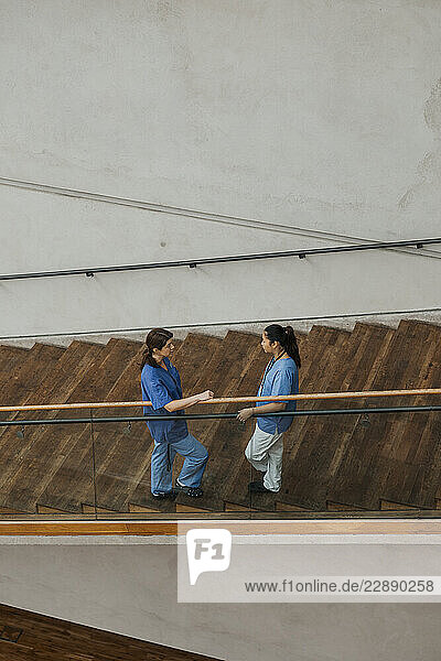 High angle view of female nurses talking with each other while standing near railing on steps in hospital building