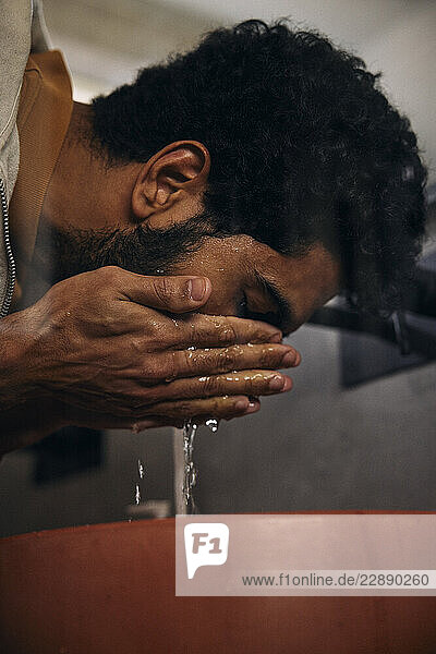 Man washing face with water in sink at bathroom