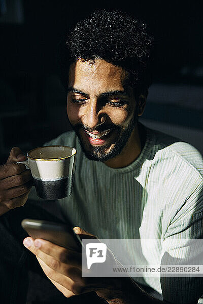 Happy man drinking coffee while using smart phone