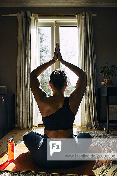 Rear view of woman with doing yoga with hand clasped while sitting at home