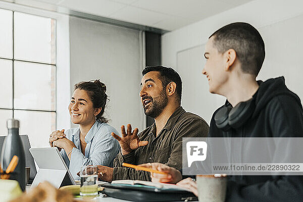 Male business professional gesturing while sitting with colleagues during meeting in tech office