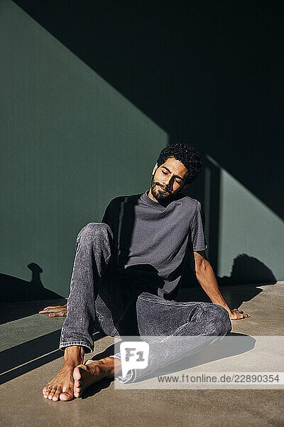 Carefree man with eyes closed sitting on floor near wall at home