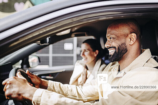Smiling bearded man driving car while enjoying with woman during road trip