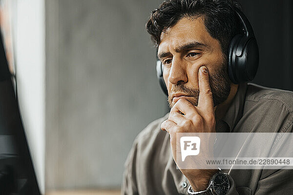 Focused male computer programmer with wireless headphones working at office