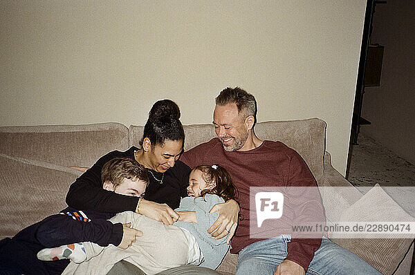 Father and mother spending leisure time with children while sitting on sofa at home