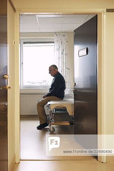 Sad senior man sitting on examination table in medical clinic