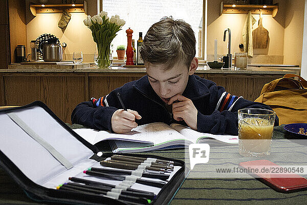 Thoughtful boy with set of colored pencils on table at home