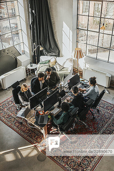 High angle view of focused multiracial software engineers working while sitting at desk in tech hub