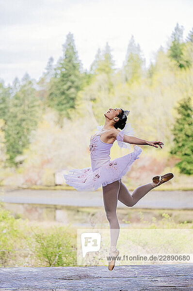 Ballerina in pink tutu dances gracefully outdoors with trees and water in the background. WA  USA