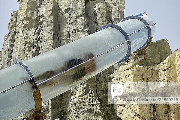 Person sliding through a clear tube slide set against rugged rocky terrain. Abu Dhabi  UAE