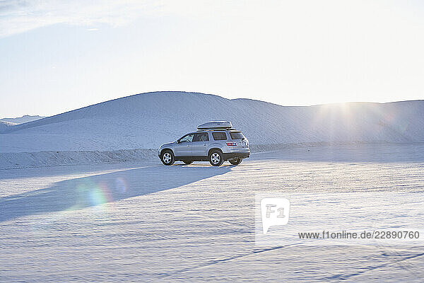 SUV driving on vast white desert landscape under a bright sunny sky. Road Trip USA