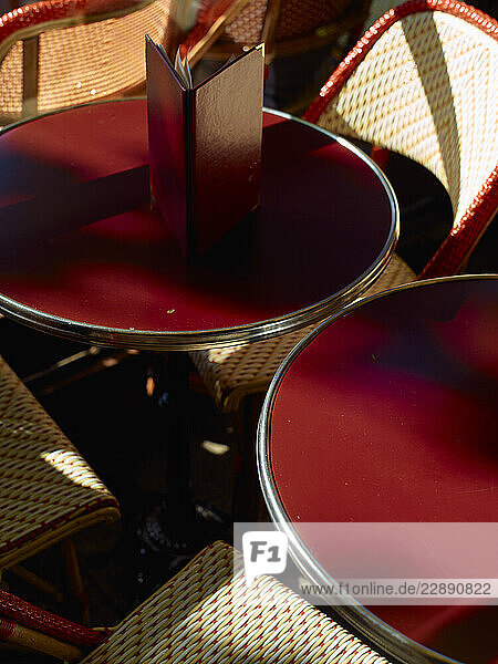 Sunlit red cafÈ tables with woven rattan chairs arranged closely around them.