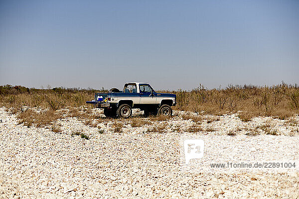 Classic blue pickup truck parked on a rocky desert landscape under a clear blue sky. Road Trip USA
