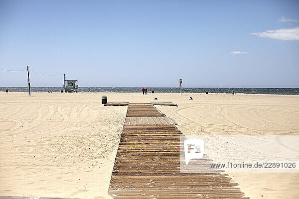 A wooden boardwalk stretches across a sandy beach leading to the ocean under a blue sky. Los Angeles  USA
