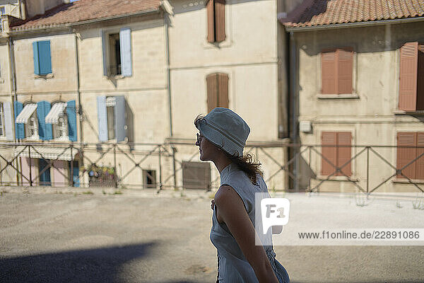 Woman in hat walks past Mediterranean-style buildings with colorful shutters.