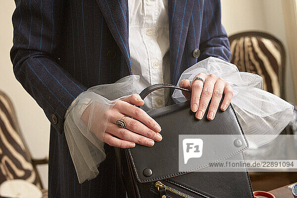 Close-up of woman in blue pinstripe suit holding a black leather handbag in an elegant setting. Germany