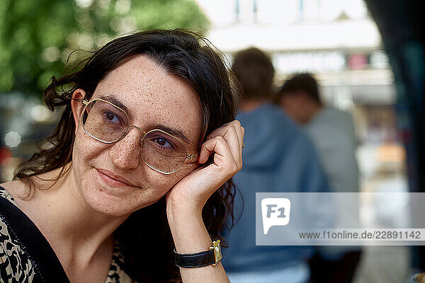 Woman with glasses smiling  resting her head on her hand in an outdoor setting.