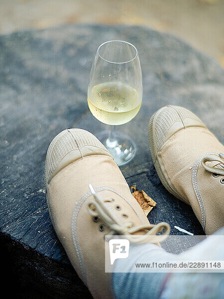 Beige sneakers on a stone surface with a glass of white wine beside them.
