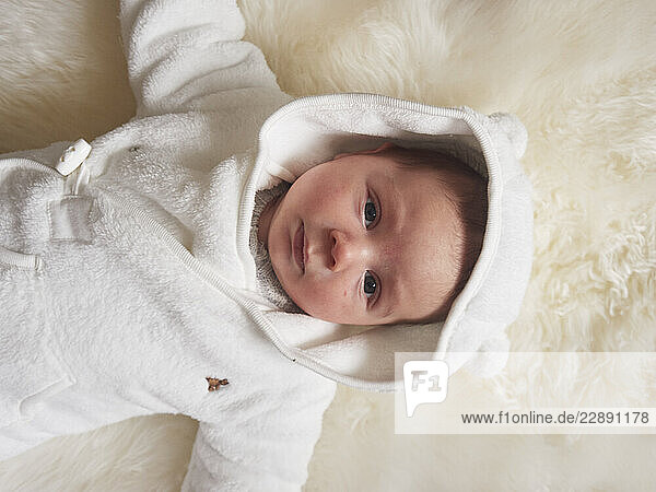 Baby lying in a white bear-themed hooded onesie on a soft cream blanket.
