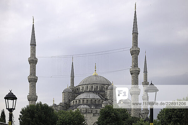 Majestic mosque with multiple minarets against a cloudy sky  surrounded by trees and lamps. Istanbul  Turkey