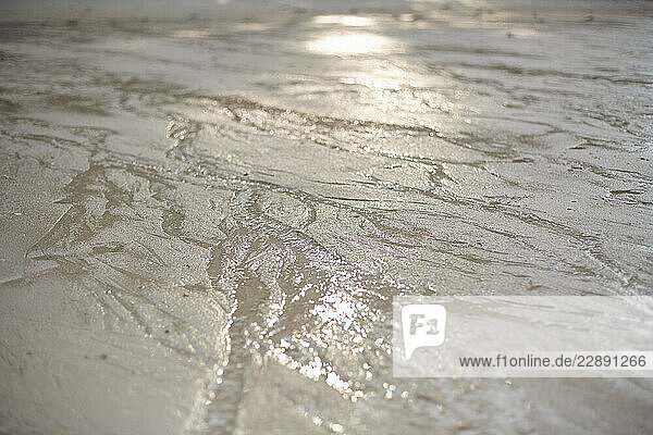 Wet sand with intricate patterns created by receding water reflecting sunlight. Thailand