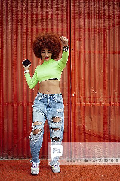 Cheerful woman dancing in front of red wall