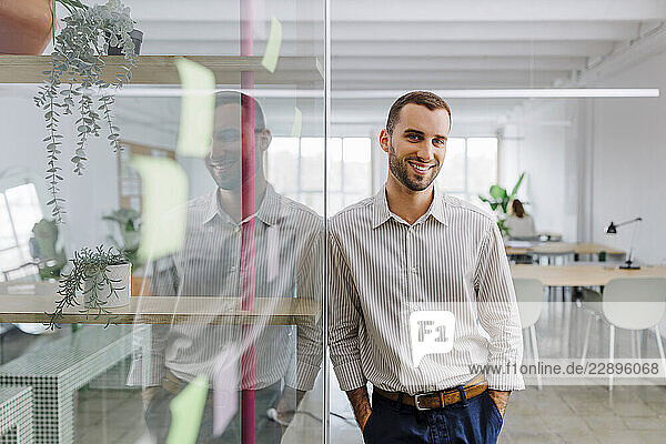 Confident businessman smiling in a modern coworking office with glass walls and sticky notes