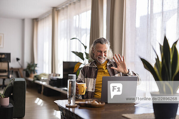 Man working from home in a modern living room  smiling and waving during a video call