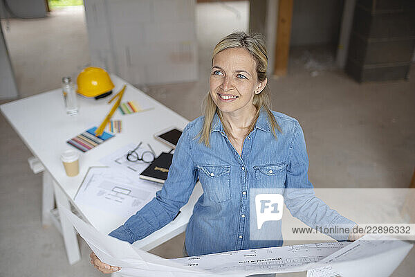 Female building contractor looking away holding blueprint at site