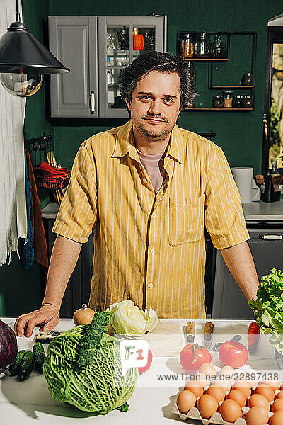 Man in a yellow shirt cooking with eco vegetables in a kitchen