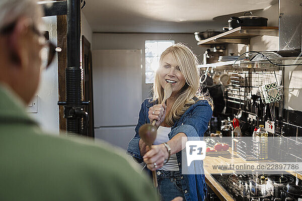 Woman playfully singing with a wooden spoon in a kitchen with a man