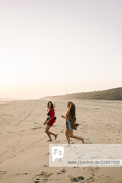 Two friends running joyfully on a beach at sunset