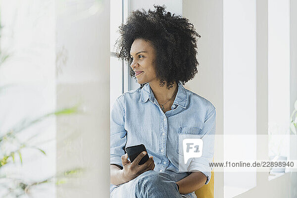 Young smiling woman with mobile phone at window