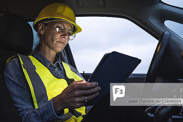 Mature female professional using digital tablet while sitting in car