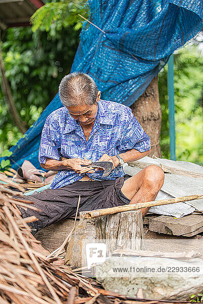 Elderly artisan shaping wood pin for broom