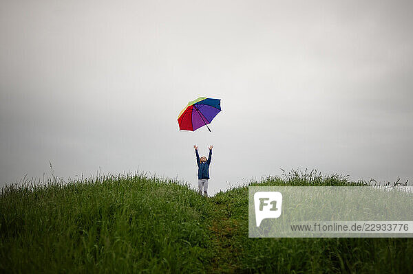 Rainbow umbrella blowing away from tween girl stormy sky